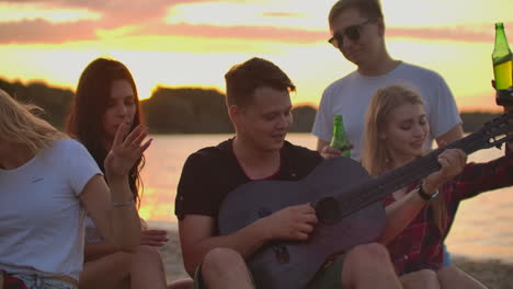 Die-Freunde-Spielen-Gitarre-Und-Singen-Lieder-Am-Lagerfeuer-Auf-Der-Strandparty.-Das-Ist-Ein-Gefühlvoller-Sommerabend-Mit-Den-Besten-Freunden-Und-Bier.